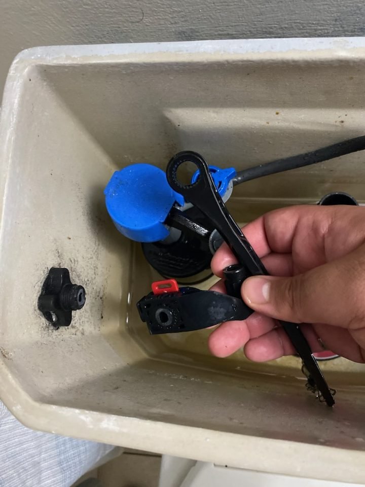 Toilet tank with the old flapper and fill valve parts removed during a running-toilet repair